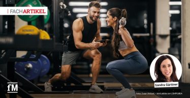 Trainer begleitet eine Trainierende beim Krafttraining mit Kurzhanteln im Fitnessstudio.