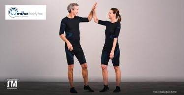 Ein Mann und eine Frau tragen enganliegende EMS-Trainingskleidung und geben sich lächelnd ein High Five vor neutralem Hintergrund