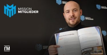 Ein Mann (Daniel Großgarten, Geschäftsführer von Mission Mitglieder) sitzt in der rechten Bildhälfte hält eine aufgeschlagene Zeitschrift mit dem Titel 'Neue Fördermitglieder' in der Hand und zeigt mit seinem rechten Zeigefinger auf den Text, vor einer schwarzen Wand mit Mission-Mitglieder-Logos (türkisfarben und weiß) in der rechten Bildhälfte. Oben links befindet sich ein großes Mission-Mitglieder-Logo und unten links in weißer Schrift das Signet 'fM'.