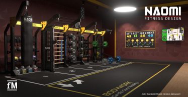 Trainingsbereich mit Boxsack links vorne, Functional-Rig mit Hanteln und Medizinbällen mittig, Bodenmarkierungen mit Pfeilen und Schrift „BODYWORK Cardio Core Mobility“, Bildschirm mit Trainingsanzeige an der Wand.