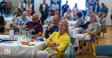 Zahlreiche Teilnehmerinnen und Teilnehmer sitzen an runden Tischen und hören konzentriert einem Vortrag beim ONE.FUTURE Netzwerktreffen zu.
