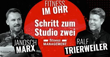 Zwei Männer (links Janosch Marx, rechts Ralf Trierweiler) sitzen sich in einem Podcaststudio gegenüber und sprechen in Mikrofone, im Hintergrund ist ein roter Kreis mit dem Schriftzug 'Fitness im Ohr' und 'Schritt zum Studio zwei' zu sehen.