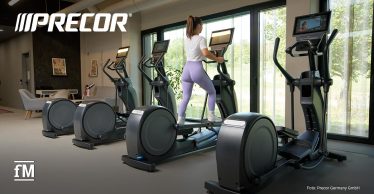 Eine Frau trainiert allein auf einem Crosstrainer vor großen Fenstern in einem hellen, modernen Fitnessbereich.