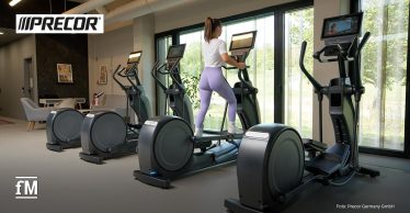 Eine Frau trainiert allein auf einem Crosstrainer vor großen Fenstern in einem hellen, modernen Fitnessbereich.