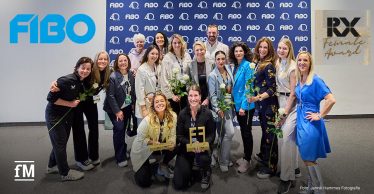 Teilnehmerinnen der Preisverleihung RX Female Award posieren zusammen mit Jurymitglied Janosch Marx mit weißen Rosen und den beiden Preisträgerinnen Frances Weber und Anna Martin-Niedecken vor einer blauen FIBO-Wand.