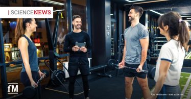 Vier Personen unterhalten sich im Fitnessstudio, zwei halten Hanteln, eine Person ein Tablet