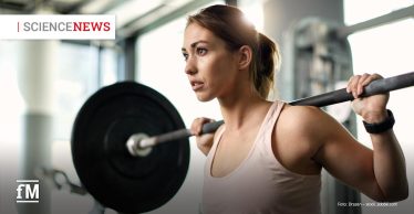 Junge Frau trainiert im Fitnessstudio mit einer Langhantel auf den Schultern, Fokus auf Konzentration und Anstrengung beim Krafttraining
