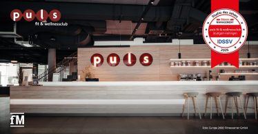 Empfangsbereich des puls fit & wellnessclubs Stuttgart-Vaihingen mit beleuchtetem Logo und moderner Tresenanlage, ausgezeichnet als 'Studio des Jahres 2025'.