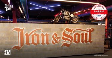 Trainingsbereich von Iron&Soul Köln mit beleuchtetem Iron&Soul-Schriftzug und Motorrad.