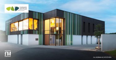 Moderne Gebäudeansicht mit großen Fenstern und bunter Fassade bei Abendlicht, Logo des Therapiezentrums sichtbar.