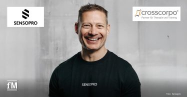 Porträt eines lachenden Mannes im schwarzen Sensopro-T-Shirt vor grauem Hintergrund. Oben sind die Logos von Sensopro und crosscorpo mit dem Zusatz
