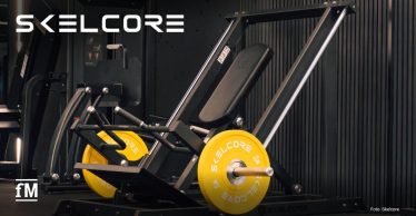 Schwarze Beinpresse mit gelben 15kg Skelcore-Gewichtsscheiben, schwarzer Wandverkleidung und Skelcore-Logo oben links im Bild.