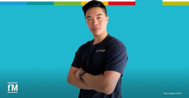 Hung Quang Nguyen steht frontal mit verschränkten Armen vor türkisem Hintergrund. Er trägt ein dunkles T-Shirt mit Integion-Logo auf der linken Brust. Oben verläuft ein mehrfarbiger Balken.