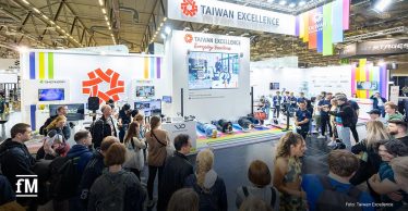 „Taiwan Excellence“-Messestand mit vielen Besuchenden; in der Mitte machen mehrere Personen auf bunten Matten Fitnessübungen.