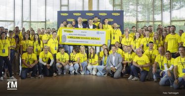 Gruppenfoto in einer Halle mit großer Fensterfront. Im Vordergrund und in der Bildmitte halten mehrere Personen einen großen symbolischen Scheck mit den Aufschriften „Technogym“, „World Food Programme“ und „1 MILLION SCHOOL MEALS“. Zahlreiche Personen tragen gelbe T-Shirts mit dem Text „LET'S MOVE FOR A BETTER WORLD“. Im Hintergrund steht eine Technogym-Bannerwand mit Logos.