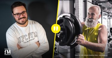 Porträt eines Mannes in einem Innenraum mit warmem Licht; im Vordergrund lächelnd, im Hintergrund unscharfer Raum mit Glasflächen