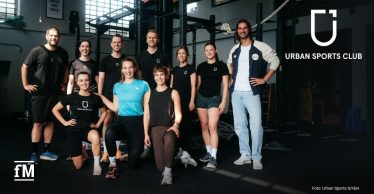 Eine Gruppe von Personen in Sportkleidung posiert in einem Fitnessstudio vor Functional Training-Geräten für ein Foto.