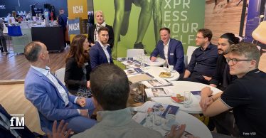 Eine Gruppe von etwa zehn Personen der sitzt im an einem runden Tisch auf der Fitnessmesse FIBO.