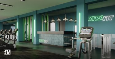 Modernes Fitnessstudio mit türkisfarbenem Design und stilvoller Beleuchtung. Im Vordergrund stehen Cardiogeräte, rechts eine Rezeption mit dem Logo 'XTRAFIT'. Helle Atmosphäre mit klaren Linien und Glasdetails.