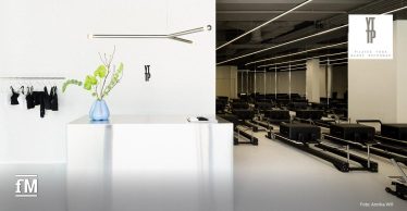 Heller Empfangsbereich und Trainingsfläche mit mehreren schwarzen Reformer-Geräten.